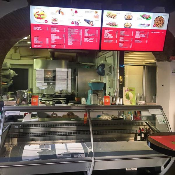 Due monitor display in 4K da 49 pollici di Samsung Smart Signage con staffaggio a soffitto espongono menu, prodotti e prezzi