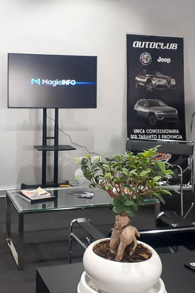 Display Samsung Smart Signage installato su supporto mobile all'interno di un auto salone, espone offerte ed annunci di auto nuove ed usate